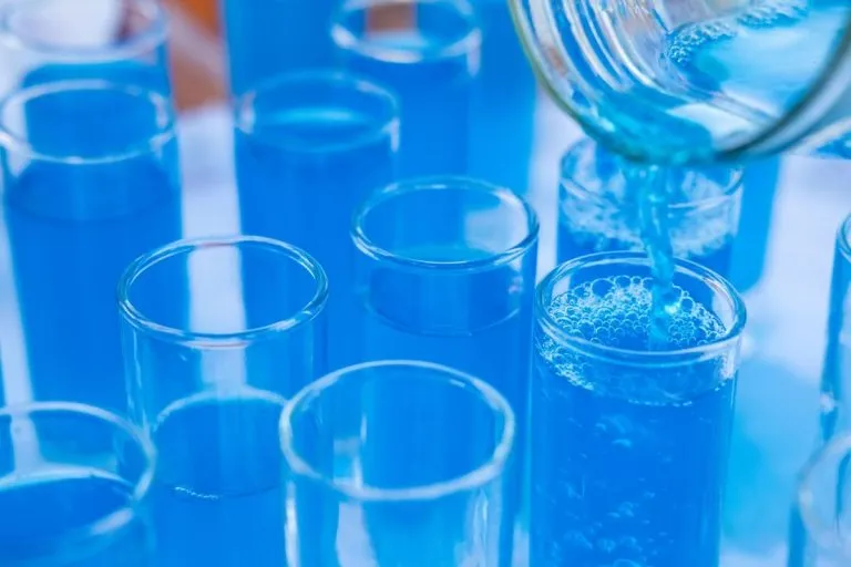 Close-up of blue liquid being poured into glass test tubes in a laboratory setting.